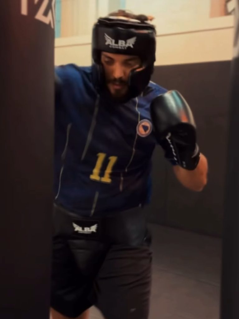 A boxer in an Alba Combat head guard, gloves and groin guard working on a heavy bag